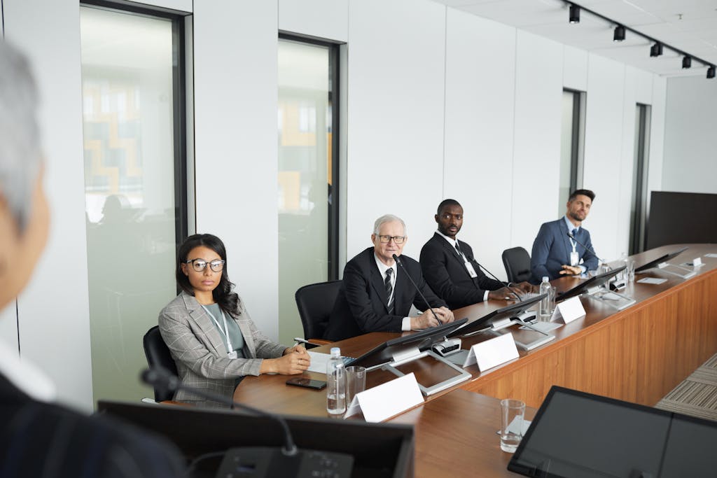 A diverse group of professionals in a modern office setting, seated around a conference table during a business meeting.